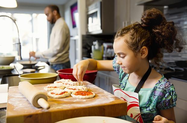 Girl making homemade pizzas with dad in the background
