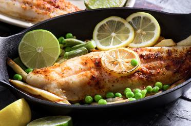 Cooked Cajun freshwater fish in a skillet with peas and lemon