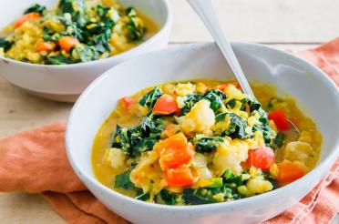 Two bowls of hearty, red lentil stew with kale on a table