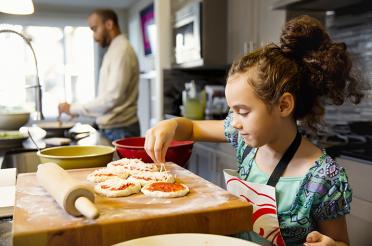 Girl making homemade pizzas with dad in the background