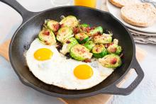 Cast iron pan with Brussels sprouts, bacon, two eggs with English muffins on the side